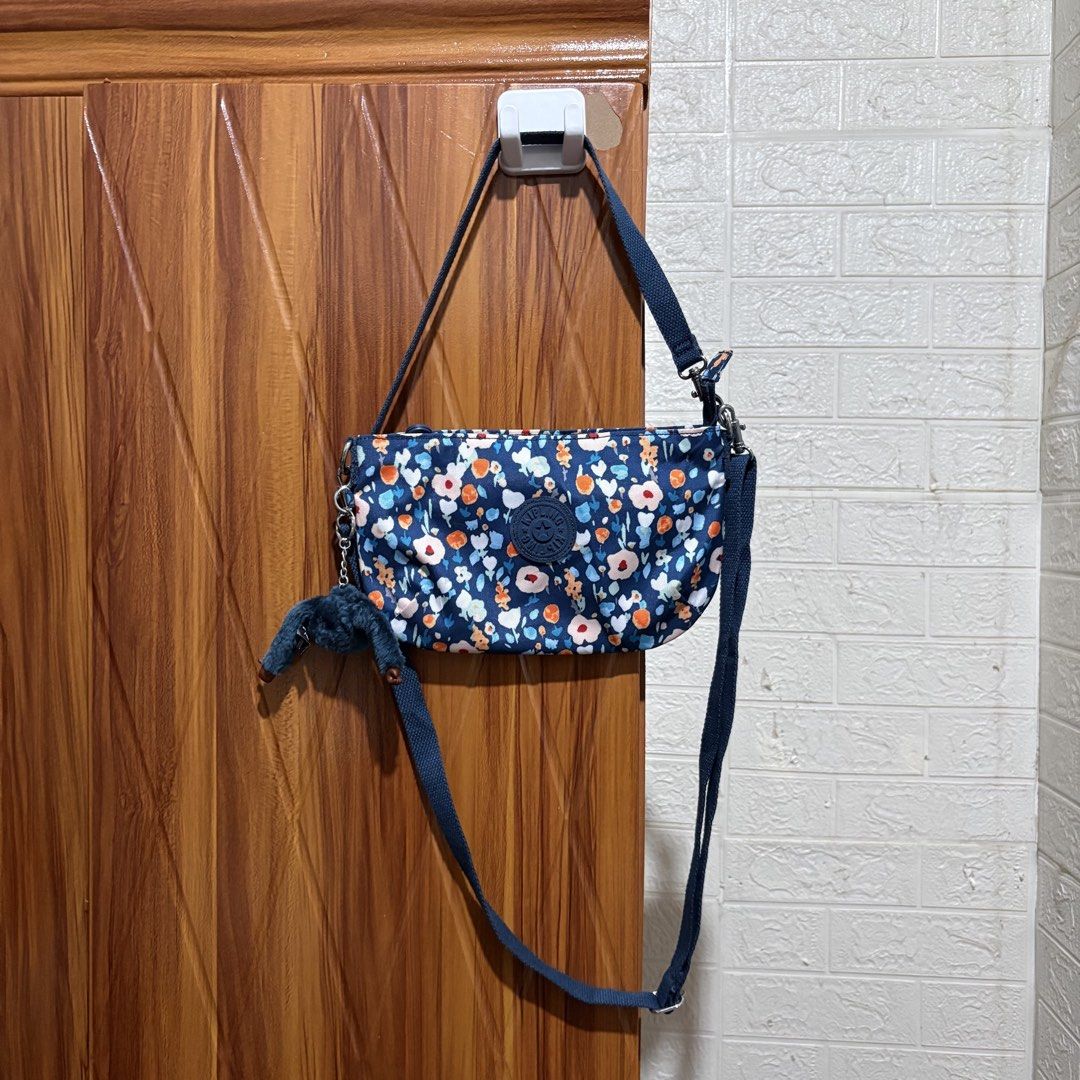 Kipling Navy Floral Crossbody Bag with Monkey Keychain (Category: Cross-body Bags) located in Carmen. Submitted by rr_thrifts (Listing ID 1464719875, Image 1). Description: - Brand: Kipling Crossbody Bag - Color/Pattern: Dark blue with an all-over colorful floral design - Included Accessory: Signature fuzzy monkey keychain - Features: Adjustable shoulder strap, top zip closure, light-colored fabric lining, and interior pockets - Condition: Excell