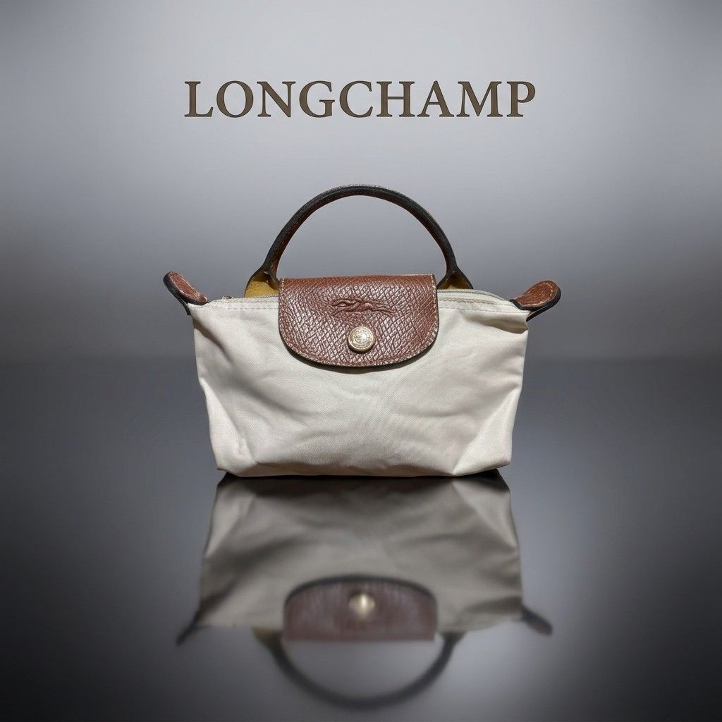 Longchamp Le Pliage Extra Small Mini Top Handle Bag (Category: Purses & Pouches) located in Carmen. Submitted by ar_thrift00 (Listing ID 1464715504, Image 1). Description: - Brand: Longchamp Mini Top Handle Bag - Color: Off-white nylon with brown leather flap - Hardware: Gold-tone with signature horse embossed pull - Closure: Zipper with front snap button flap - Interior: Clean lining with open pocket for organization - Size: Compact, perfect for