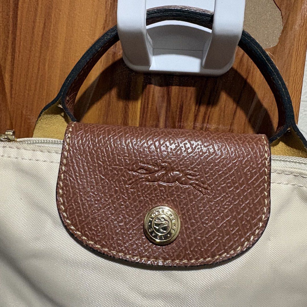 Longchamp Le Pliage Mini Handbag Beige Brown (Category: Purses & Pouches) located in Carmen. Submitted by rr_thrifts (Listing ID 1464720615, Image 2). Description: -Mini Longchamp Le Pliage bag - Elegant beige canvas body with durable brown leather handle and flap - Classic gold-tone front snap button closure - Secure zip top with signature circular Longchamp zipper pull - Compact size, ideal for carrying small daily essentials.
