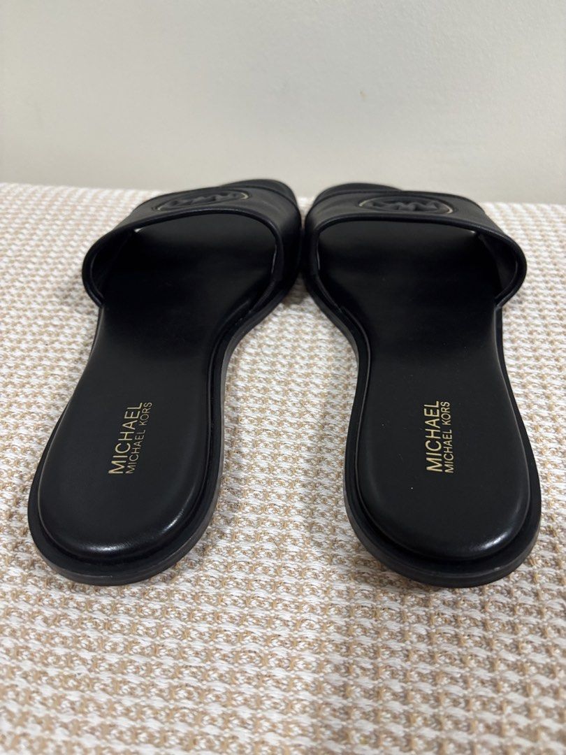 Michael Kors Black Slides Sandals with MK Logo (Category: Flats & Sandals) located in Dasmarinas. Submitted by gueenclaire (Listing ID 1464729966, Image 3). Description: Michael Kors black slide sandals. Classic slip-on style with a wide strap across the top. Features the iconic MK circular logo hardware in black and gold tone. Padded black footbed with gold Michael Kors stamp branding. Low heel design. Clean soles and edges. Size 8.5 slightly us