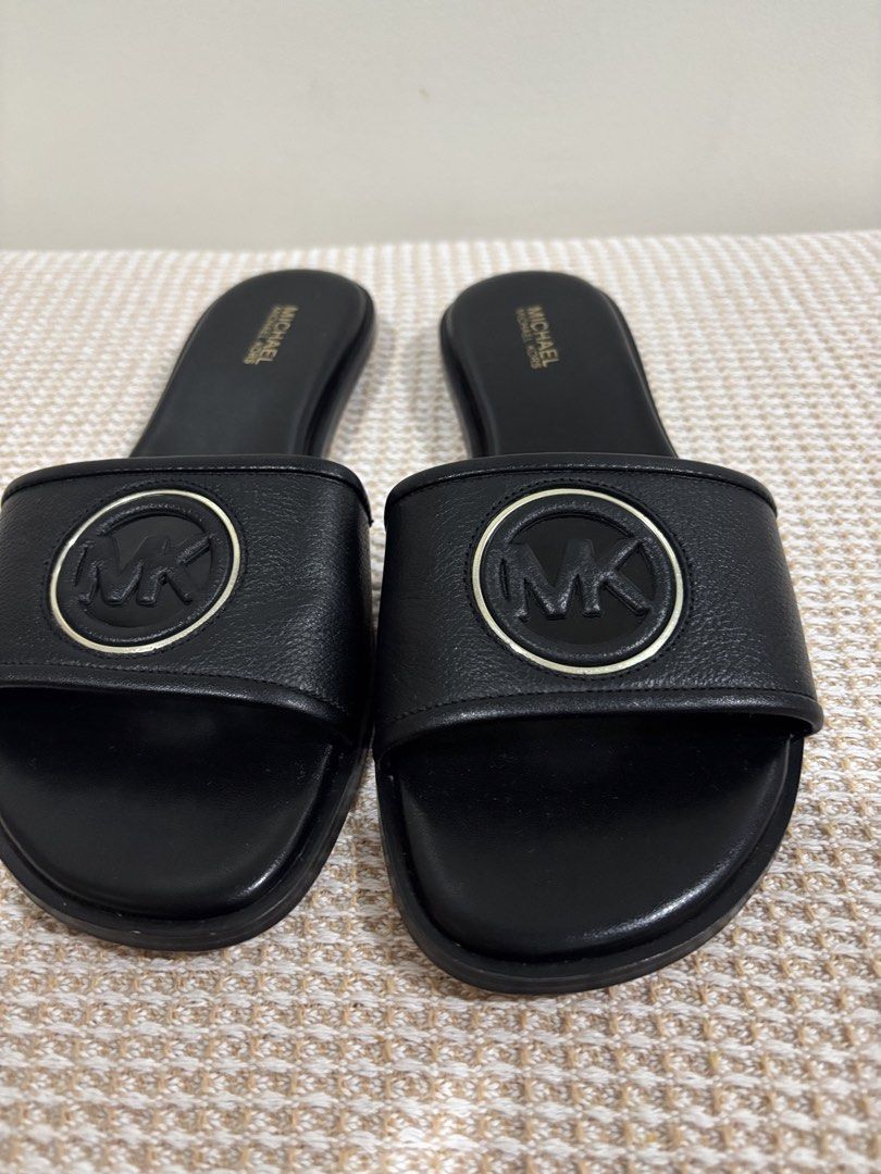 Michael Kors Black Slides Sandals with MK Logo (Category: Flats & Sandals) located in Dasmarinas. Submitted by gueenclaire (Listing ID 1464729966, Image 2). Description: Michael Kors black slide sandals. Classic slip-on style with a wide strap across the top. Features the iconic MK circular logo hardware in black and gold tone. Padded black footbed with gold Michael Kors stamp branding. Low heel design. Clean soles and edges. Size 8.5 slightly us