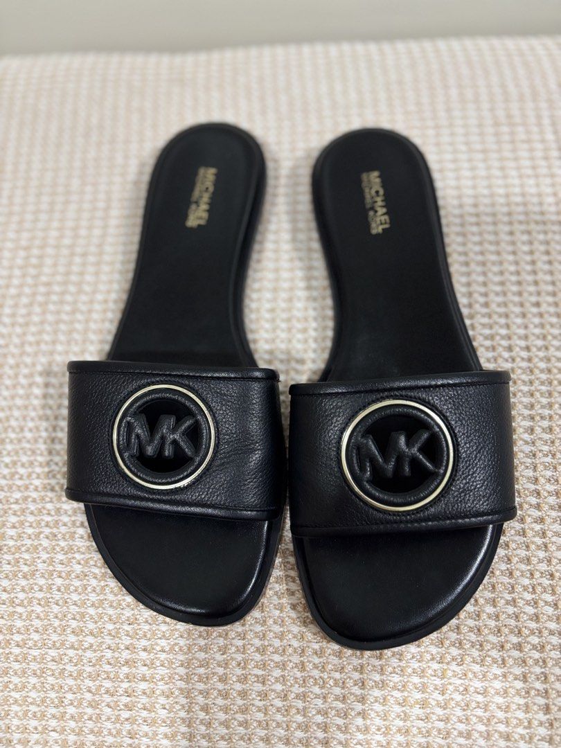 Michael Kors Black Slides Sandals with MK Logo (Category: Flats & Sandals) located in Dasmarinas. Submitted by gueenclaire (Listing ID 1464729966, Image 1). Description: Michael Kors black slide sandals. Classic slip-on style with a wide strap across the top. Features the iconic MK circular logo hardware in black and gold tone. Padded black footbed with gold Michael Kors stamp branding. Low heel design. Clean soles and edges. Size 8.5 slightly us
