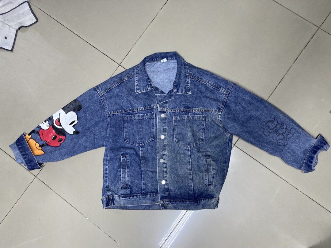 Mickey Mouse Denim Jacket (Category: Coats, Jackets and Outerwear) located in Bulacan. Submitted by fordypao (Listing ID 1464593197, Image 2). Description: - Classic blue denim jacket - Big Mickey Mouse graphic on the back - Mickey Mouse details on the sleeves - Button-up front closure - Functional front pockets - Ideal for Disney enthusiasts - Unique and eye-catching design.