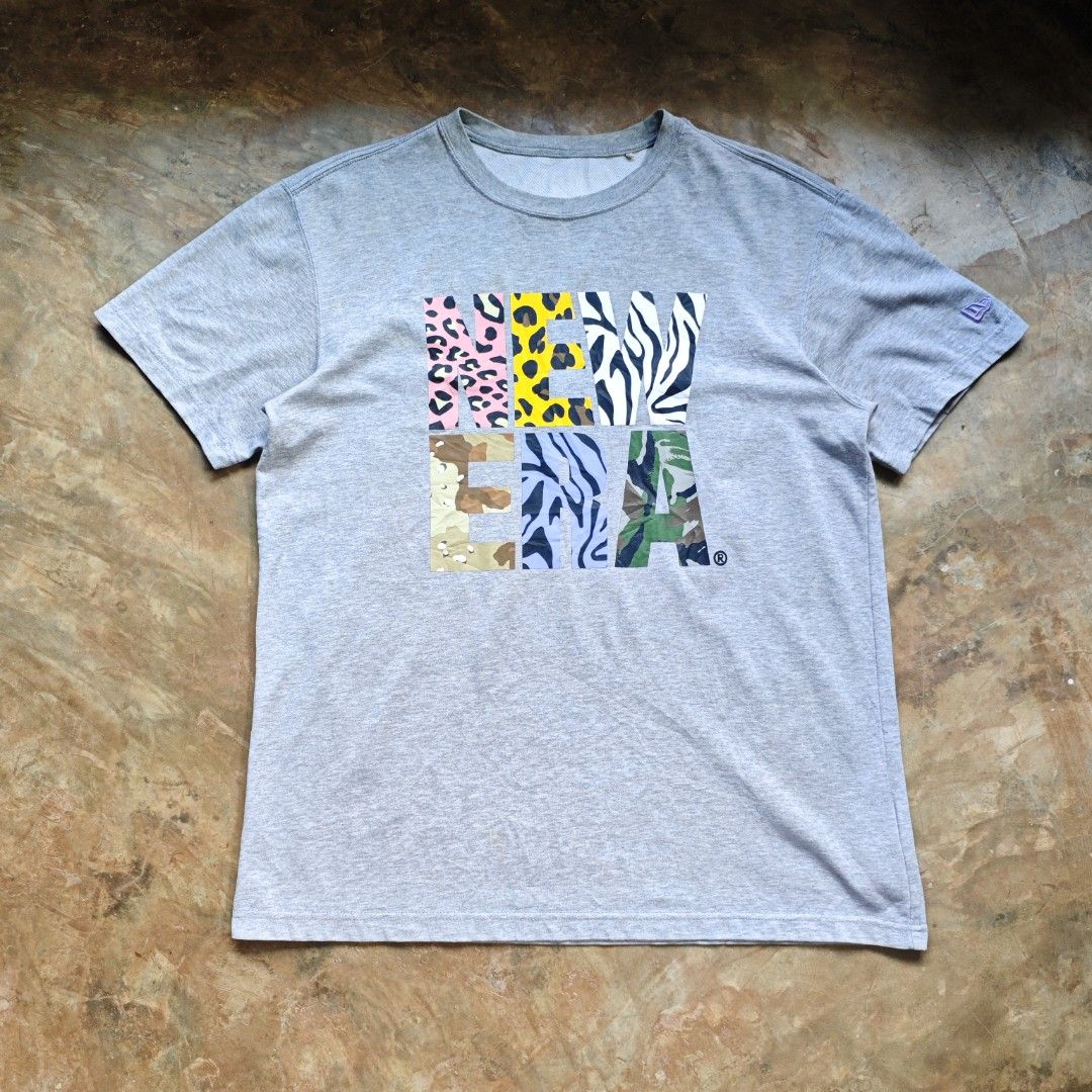 New Era T-Shirt Grey Mix Pattern Logo (Category: Tshirts & Polo Shirts ) located in Ipil. Submitted by ajthriftfinds (Listing ID 1464634681, Image 1). Description: - W: 21.5 - L: 28 - Good condition - Konting scratch sa likod ng neck and small stain need wash - Features a unique animal and camouflage print New Era logo - Tagged as 100(L) - please check measurements for accurate fit - Ideal for casual everyday wear.