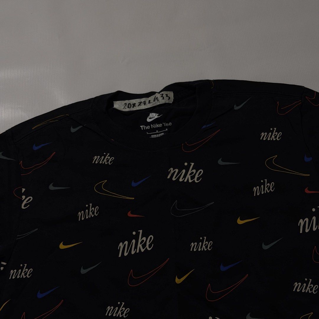 Nike All Over Print Multi Swoosh Tee Black (Category: Tshirts & Polo Shirts ) located in Manila. Submitted by johnedel_james (Listing ID 1464699234, Image 2). Description: - Brand: Nike - Condition: Brand new with interior tags intact - Size: Large (L) - Color: Black with multi-color all-over swoosh and script print - Material: 100% Cotton - Details: Short sleeves, crew neck, and vintage-style orange swoosh logo patch on the left sleeve - Origin: