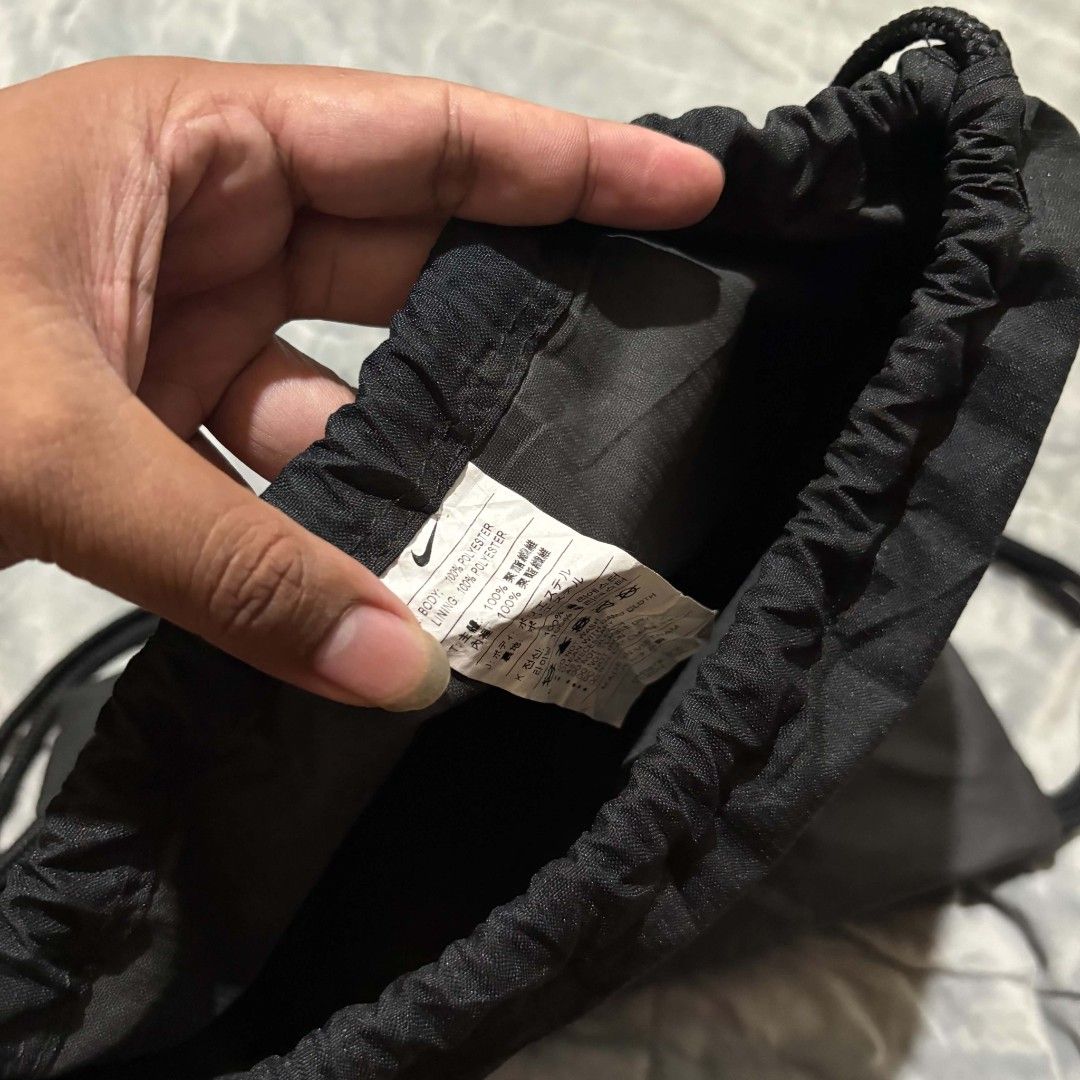 Nike Black Drawstring Gym Bag (Category: Backpacks) located in Carmen. Submitted by ar_thrift00 (Listing ID 1464715334, Image 3). Description: Black Nike drawstring backpack, 100% polyester body and lining. Large white swoosh on front. Vertical zip pocket on the side, plus a handy top grab handle. Drawstring cords work smoothly. Clean inside tag showing material breakdown. Great daily gym or school sack..