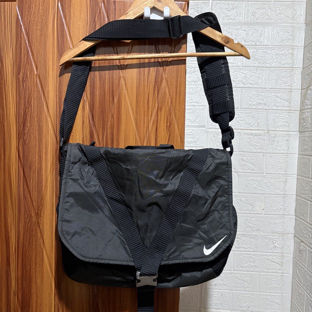 Nike Black Messenger Bag with Adjustable Strap and Buckle (Category: Sling Bags) located in Carmen. Submitted by rr_thrifts (Listing ID 1464722165, Image 1). Description: - Brand/Item: Black Nike Messenger Bag - Material: Durable nylon that holds its shape well - Design: Front flap with white Nike swoosh, secure buckle closure, and strap with repeated Nike lettering - Storage: Interior zippered pockets and organizational compartments - Versatilit