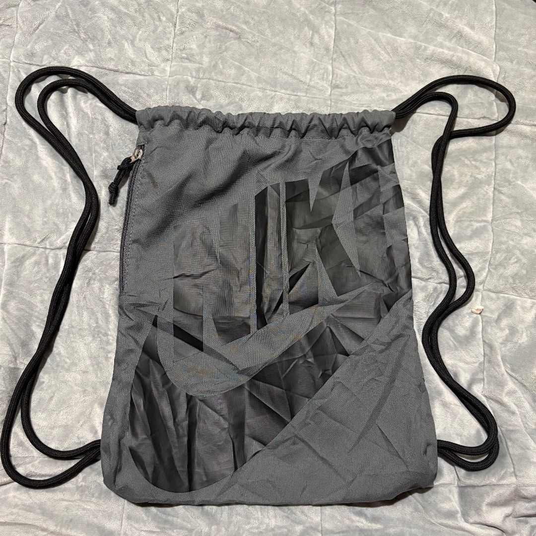 Nike Grey Drawstring Gym Bag with Zipper Pocket (Category: Backpacks) located in Carmen. Submitted by rr_thrifts (Listing ID 1464722963, Image 1). Description: - Brand: Nike - Color: Grey with large geometric graphic print - Material: 100% polyester (verified by inside tag) - Storage: Spacious main compartment with drawcord closure plus a secure side zipper pocket - Design: Lightweight, packable, and easy to carry - Condition: Excellent / Ready t