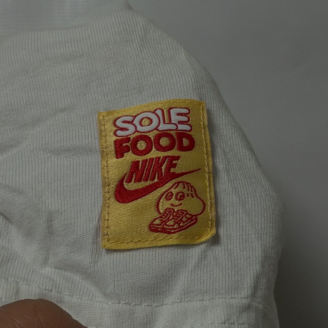 Nike Sole Food Served Fresh Dumpling Graphic Tee (Category: Tshirts & Polo Shirts ) located in Manila. Submitted by johnedel_james (Listing ID 1464708185, Image 2). Description: - Brand: Nike - Style Code: FB9804-100 - Color: White with red Swoosh and fun dumpling graphic - Text: 'SERVED FRESH' on front, 'SOLE FOOD' yellow patch on sleeve - Size: Medium (approx. 95cm chest) - Material: 100% premium cotton - Condition: Brand new.