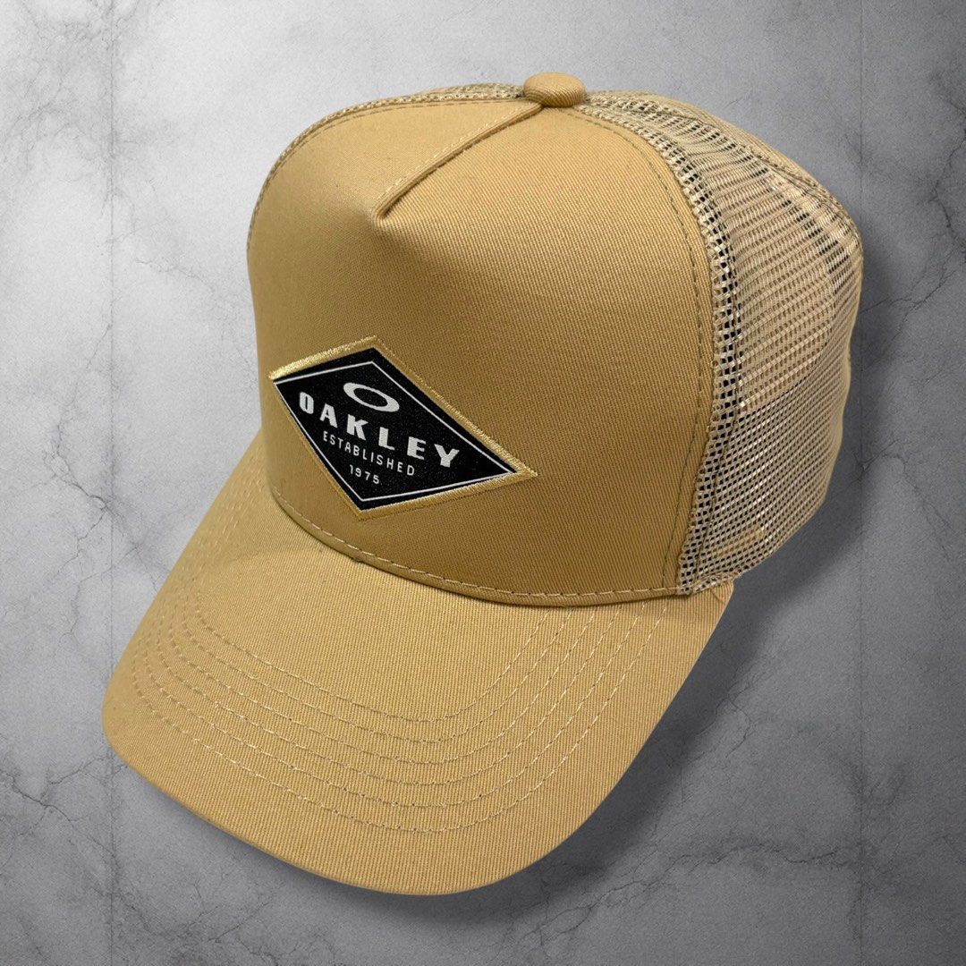 Oakley Established 1975 Trucker Hat Tan (Category: Caps & Hats) located in Cavite. Submitted by itsayaaa (Listing ID 1464698995, Image 1). Description: - Brand: Oakley - Color: Tan - Design: Diamond patch logo with 'Oakley Established 1975' in black and white - Material: Breathable mesh back panels - Brim: Curved with tonal stitching - Closure: Adjustable snapback - Condition: Clean piece, ready to wear.