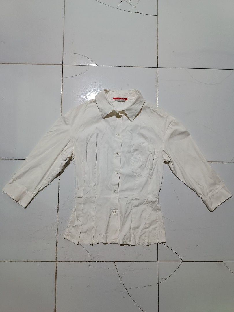 Prada White Button-Up Blouse Size 40 (Category: Blouses) located in Barotac Nuevo. Submitted by gray101 (Listing ID 1464700964, Image 1). Description: - Brand: Prada - Color: Clean white - Size: 40 - Material: Cotton blend (with nylon and elastane) - Origin: Made in Romania - Design: Button-up front, pleated waist details, and chest pocket - Sleeves: Three-quarter length with cuffed wrists - Fit: Classic tailored fit.