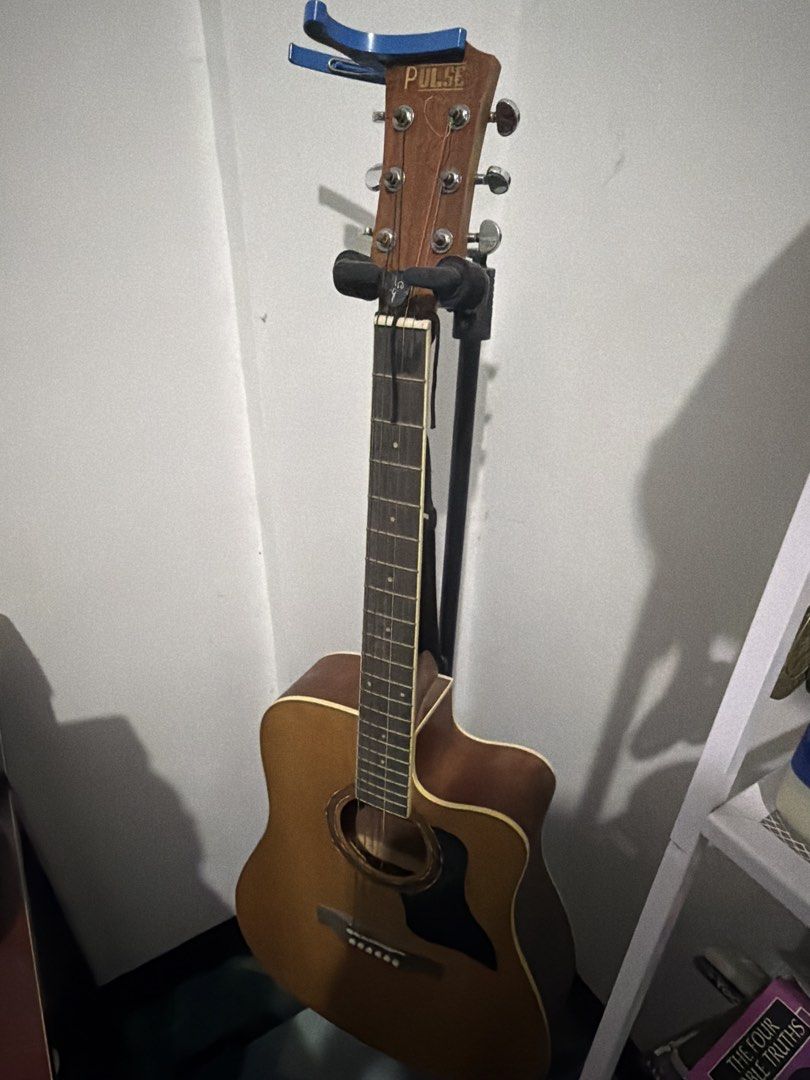 Pulse Acoustic Guitar (Category: Musical Instruments) located in Manila. Submitted by ramonrueda37147 (Listing ID 1464594387, Image 2). Description: - Acoustic guitar with "PULSE" headstock. - Six tuning pegs and strings. - Includes a blue capo. - Fretboard visible. -Free guitar stand -missing #1 - Free Guitar Stand .