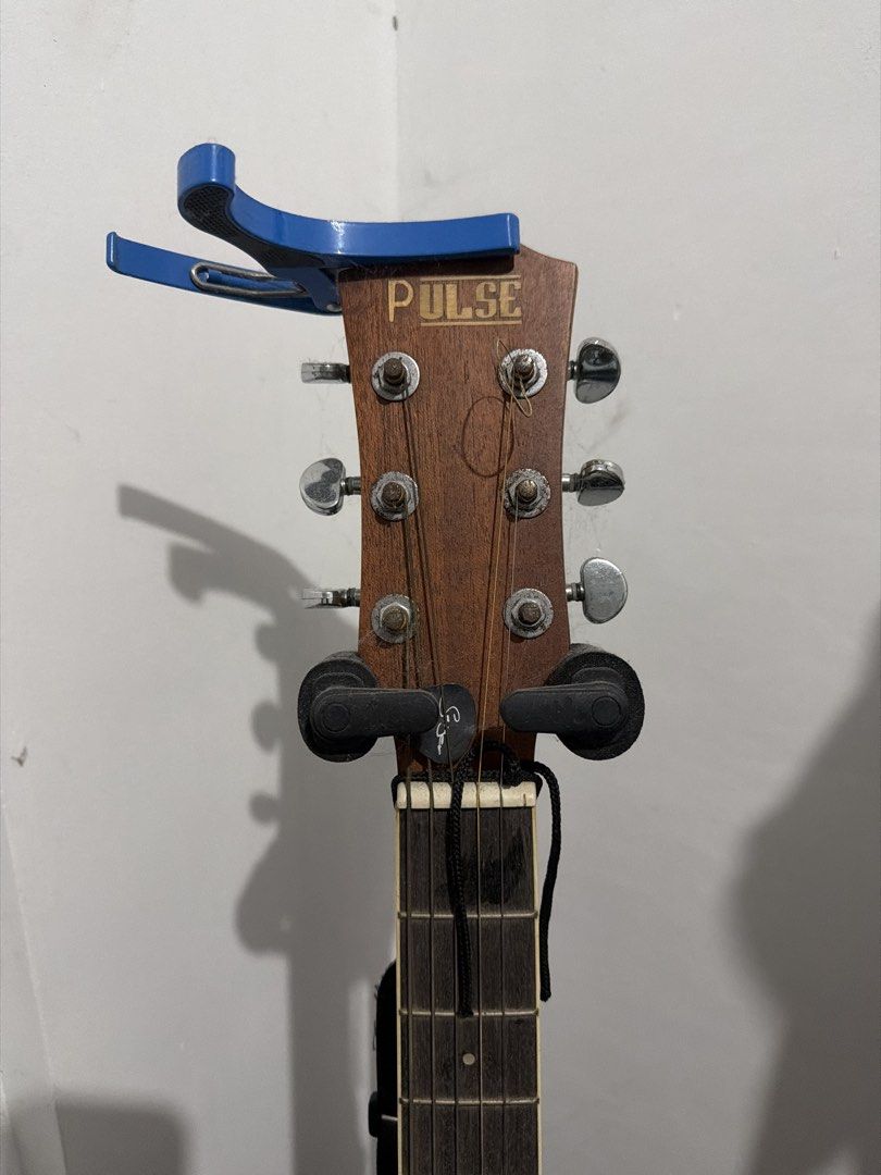 Pulse Acoustic Guitar (Category: Musical Instruments) located in Manila. Submitted by ramonrueda37147 (Listing ID 1464594387, Image 1). Description: - Acoustic guitar with "PULSE" headstock. - Six tuning pegs and strings. - Includes a blue capo. - Fretboard visible. -Free guitar stand -missing #1 - Free Guitar Stand .