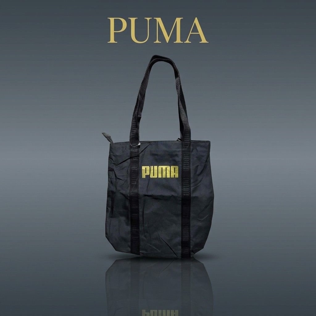 Puma Black Tote Bag with Gold Logo (Category: Tote Bags) located in Carmen. Submitted by ar_thrift00 (Listing ID 1464713112, Image 1). Description: Black Puma tote bag sporting a gold logo on the front. Double carrying handles made of sturdy webbing. Zipper closure across the top to keep your items secure. Inside lining features Puma branding pattern with an extra zippered pocket for smaller essentials. Generous space for daily errands, gym gear,