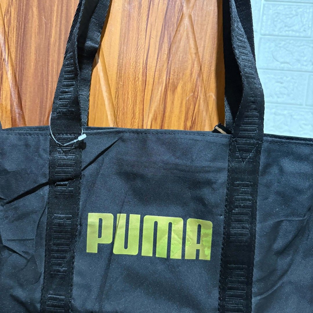 Puma Black Tote Bag with Gold Logo (Category: Tote Bags) located in Carmen. Submitted by ar_thrift00 (Listing ID 1464713112, Image 2). Description: Black Puma tote bag sporting a gold logo on the front. Double carrying handles made of sturdy webbing. Zipper closure across the top to keep your items secure. Inside lining features Puma branding pattern with an extra zippered pocket for smaller essentials. Generous space for daily errands, gym gear,