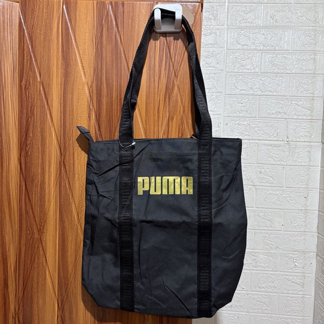 Puma Black Tote Bag with Gold Logo (Category: Tote Bags) located in Carmen. Submitted by rr_thrifts (Listing ID 1464720525, Image 1). Description: - Brand: Puma - Color: Black with striking gold logo - Closure: Secure top zipper closure - Straps: Durable black fabric straps extending down the body - Interior: Puma branded lining pattern with a convenient zippered pocket for small valuables - Versatility: Roomy everyday carryall, perfect for gym g