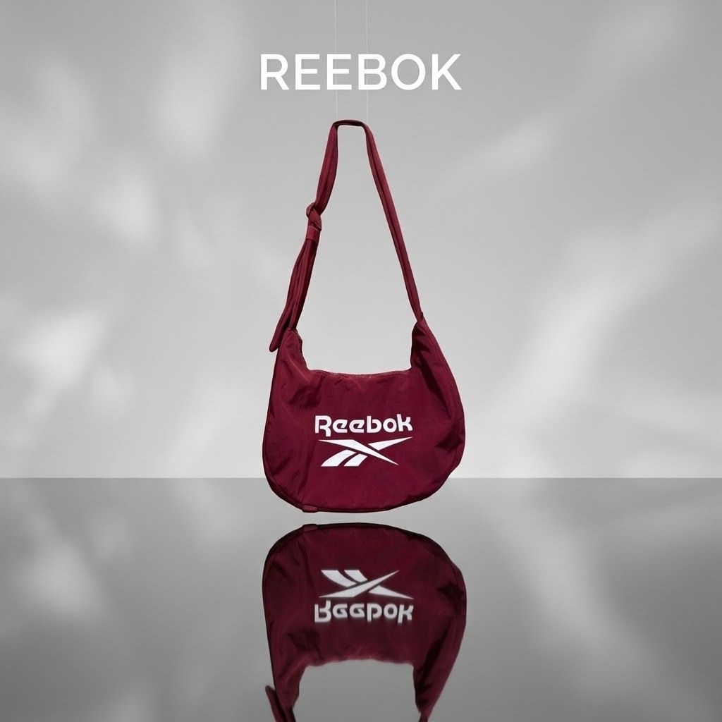 Reebok Maroon Crossbody Shoulder Bag (Category: Cross-body Bags) located in Carmen. Submitted by ar_thrift00 (Listing ID 1464711512, Image 1). Description: - Brand: Reebok - Color: Maroon with bold white front logo - Material: Lightweight nylon with deep burgundy interior lining - Strap: Adjustable shoulder strap with stylish patterned pull cord zipper detail - Storage: Main compartment plus an extra internal zipped pocket and brand tag patch - C
