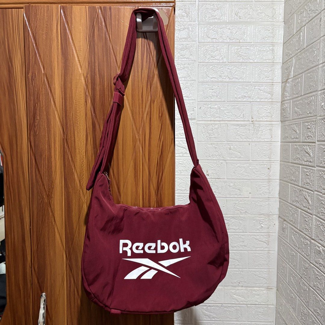 Reebok Maroon Crossbody Shoulder Bag (Category: Cross-body Bags) located in Carmen. Submitted by rr_thrifts (Listing ID 1464718590, Image 1). Description: - Brand: Reebok - Color: Maroon with large white logo on front - Material: Durable fabric with clean interior and exterior - Closure: Smooth-running top zipper - Storage: Includes an inner zippered pocket - Strap: Adjustable for comfortable wear - Origin: Made in China.