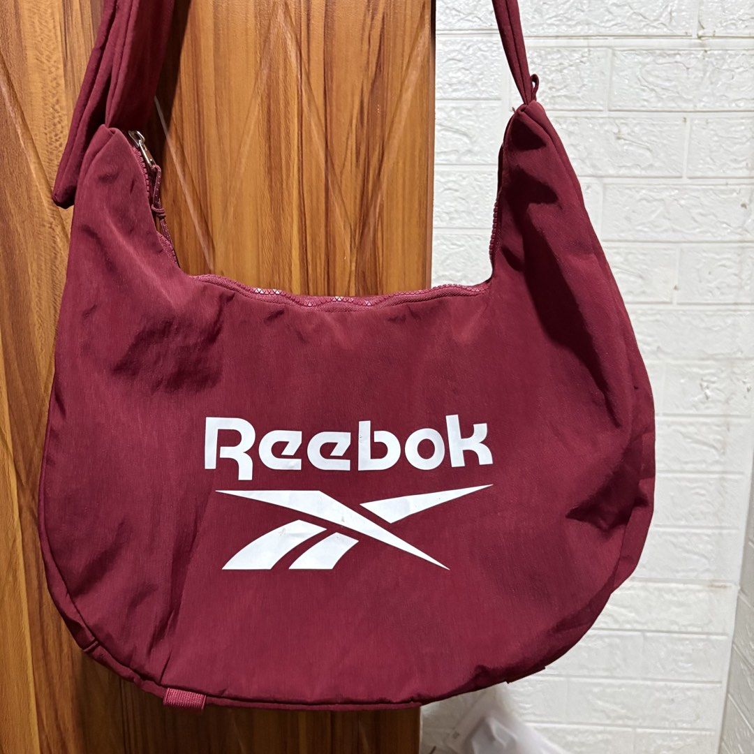 Reebok Maroon Crossbody Shoulder Bag (Category: Cross-body Bags) located in Carmen. Submitted by rr_thrifts (Listing ID 1464718590, Image 2). Description: - Brand: Reebok - Color: Maroon with large white logo on front - Material: Durable fabric with clean interior and exterior - Closure: Smooth-running top zipper - Storage: Includes an inner zippered pocket - Strap: Adjustable for comfortable wear - Origin: Made in China.