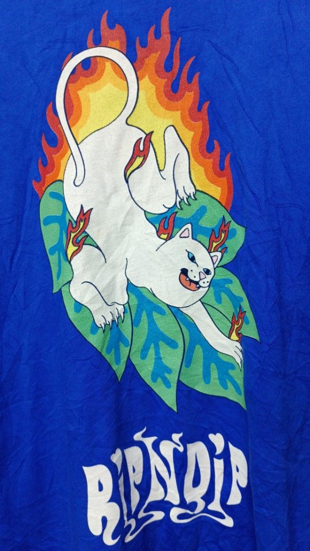RIPNDIP Blue Graphic T-shirt (Category: Tshirts & Polo Shirts ) located in Manila. Submitted by zariyah.1986 (Listing ID 1464756143, Image 3). Description: Bright blue RIPNDIP tee with a small logo hit on the front chest. Back has a large graphic of the white cat surrounded by flames and green leaves. Standard crewneck and short sleeves. Tag says size Large, measures approximately 21 inches pit to pit by 29 inches length. Cotton fabric, soft feel