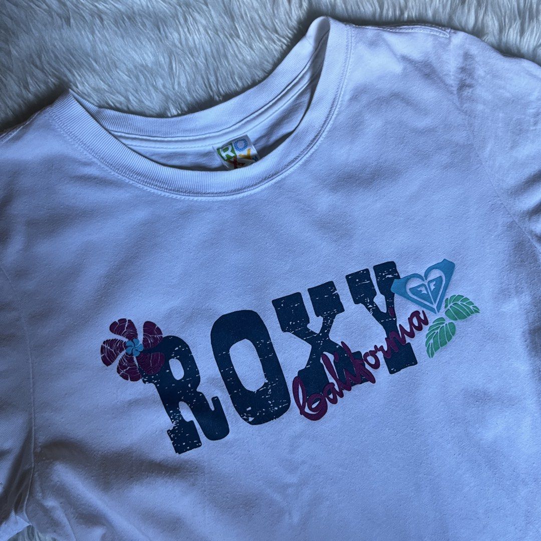 Roxy California Surf Graphic Shirt (Category: Shirts) located in Maasin. Submitted by taraa18 (Listing ID 1464591089, Image 2). Description: - White Roxy t-shirt - Features 'Roxy California' graphic on the front - Back graphic: 'Roxy Surf California Longboard Boardriding 1990' - Short sleeves and crew neck - Ideal for casual wear or beach outings.