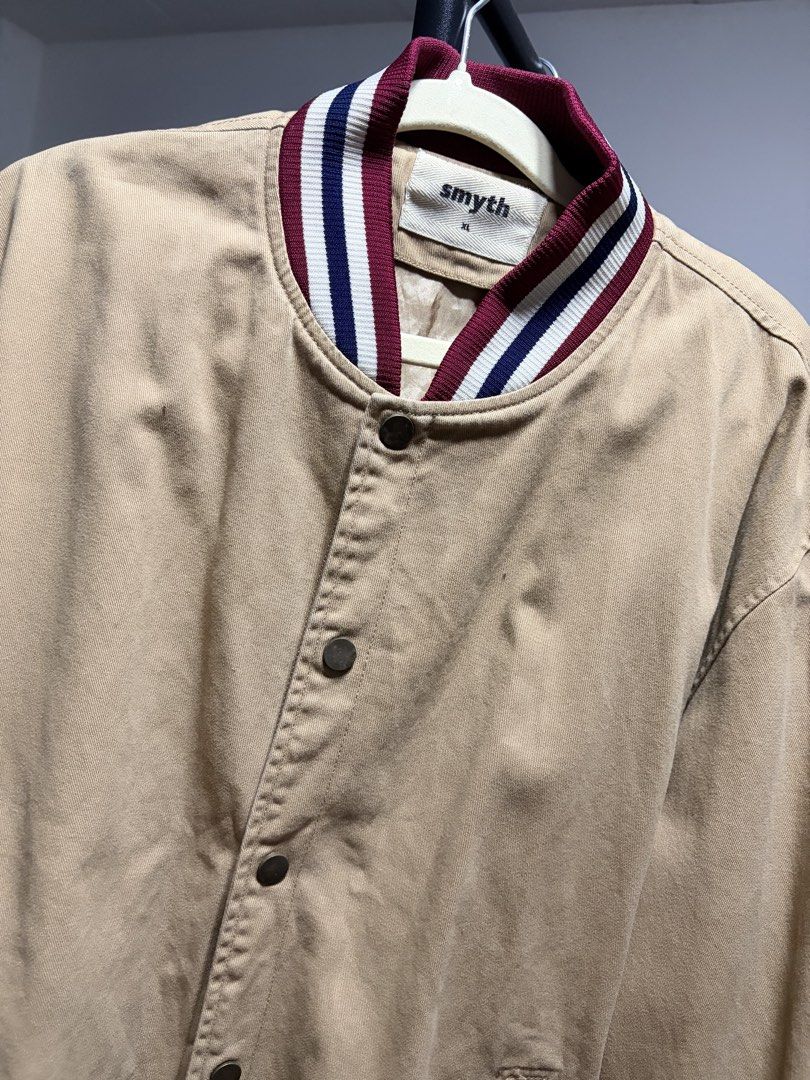 Smyth Varsity Bomber Jacket Tan Khaki Size XL (Category: Coats, Jackets and Outerwear) located in Manila. Submitted by finderskeepersmnl_092026 (Listing ID 1464744169, Image 2). Description: - Brand/Style: Smyth tan khaki varsity jacket with a classic collegiate aesthetic - Size: XL - Details: Maroon, white, and blue striped ribbing on the collar, cuffs, and hem - Closure: Snap button front - Pockets: Two vertical front pockets - Material: Sturdy