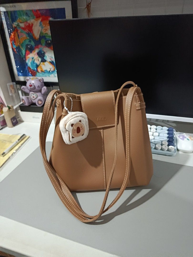 Soleia Brown Leather Shoulder Bag with Koala Charm (Category: Shoulder Bags) located in Pasay City. Submitted by pitchiiieee_ (Listing ID 1464738159, Image 1). Description: - Brand: Soleia - Material: Smooth brown leather with white contrast stitching - Closure & Straps: Front flap closure with double shoulder straps - Interior: Open pocket for small essentials - Inclusions: Fluffy koala plushie keychain and original orange brand card tag.