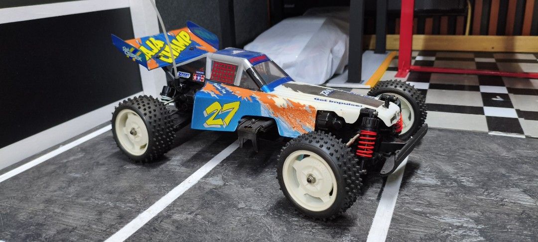 Tamiya Baja Champ RC Car (Category: Remote Control Toys) located in Caloocan City. Submitted by Outlaw (Listing ID 1464592132, Image 1). Description: - Tamiya Baja Champ remote control car - Eye-catching blue and orange livery with '27' and 'BAJA CHAMP' graphics - Shows some signs of use on body and tires, adding character - Underside view reveals chassis, motor, and servo - Ready for exciting off-road adventures - Perfect for RC car collectors a