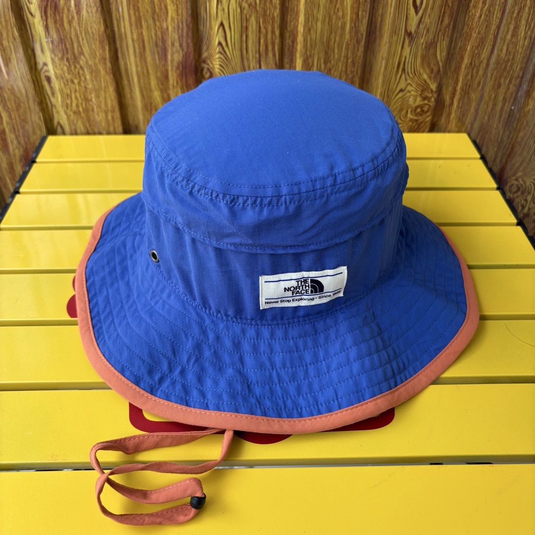 The North Face Bucket Hat Blue Orange (Category: Caps & Hats) located in Dapitan. Submitted by payt3es_thrift. (Listing ID 1464602265, Image 1). Description: - Brand: The North Face - Color: Cool Blue - Features: Orange trim, drawstring, mesh side panels for ventilation - Slogan: "Never Stop Exploring" on tag - Ideal for: Sunny days, hiking, casual wear.