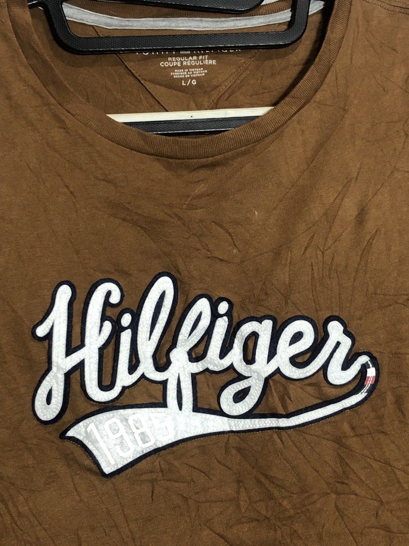 Tommy Hilfiger Brown Script Logo T-Shirt Size L (Category: Tshirts & Polo Shirts ) located in Montevista. Submitted by rdthriftshub (Listing ID 1464756008, Image 2). Description: - Brand: Tommy Hilfiger - Style: Regular fit crew neck t-shirt - Color: Brown - Size: L/G - Material: 100% cotton (Made in Vietnam) - Design: Large embroidered white script logo with '1985' on the chest - Details: Contrast inner neck taping and inner side wash tag - Cond