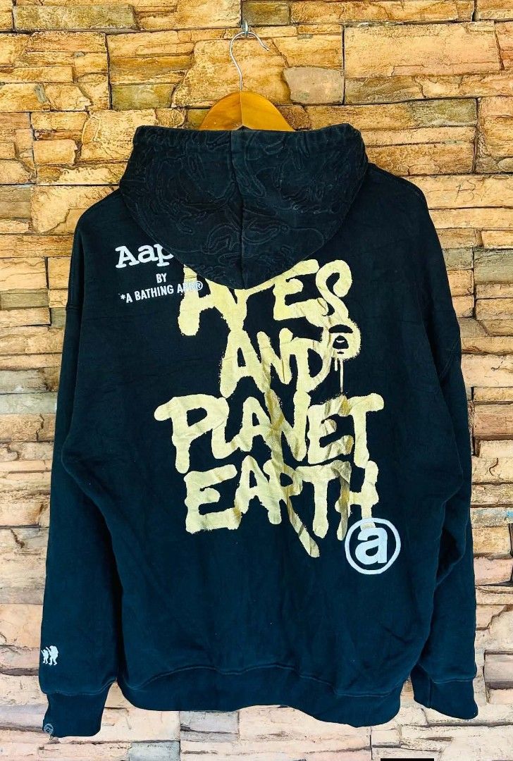 Aape By A Bathing Ape Hoodie (Category: Coats, Jackets and Outerwear) located in Santiago. Submitted by reyibanez253969 (Listing ID 1464910551, Image 2). Description: - Color: Black with striking gold graphic print on chest and back - Medium - 23x27 - Material: Comfortable 79.6% cotton and 20.4% polyester blend - Design: Features 'Aape By A Bathing Ape' and 'Yes And Planet Earth' text details - Details: Branded drawstrings, front kangaroo pocket 