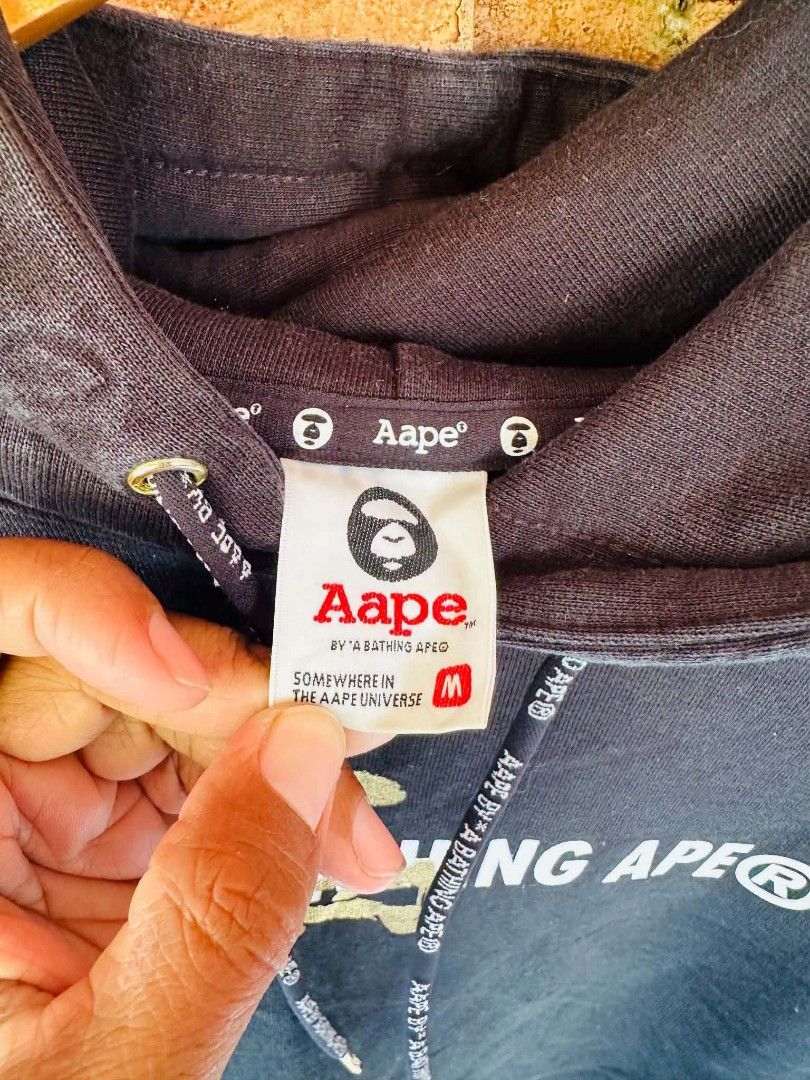 Aape By A Bathing Ape Hoodie (Category: Coats, Jackets and Outerwear) located in Santiago. Submitted by reyibanez253969 (Listing ID 1464910551, Image 3). Description: - Color: Black with striking gold graphic print on chest and back - Medium - 23x27 - Material: Comfortable 79.6% cotton and 20.4% polyester blend - Design: Features 'Aape By A Bathing Ape' and 'Yes And Planet Earth' text details - Details: Branded drawstrings, front kangaroo pocket 