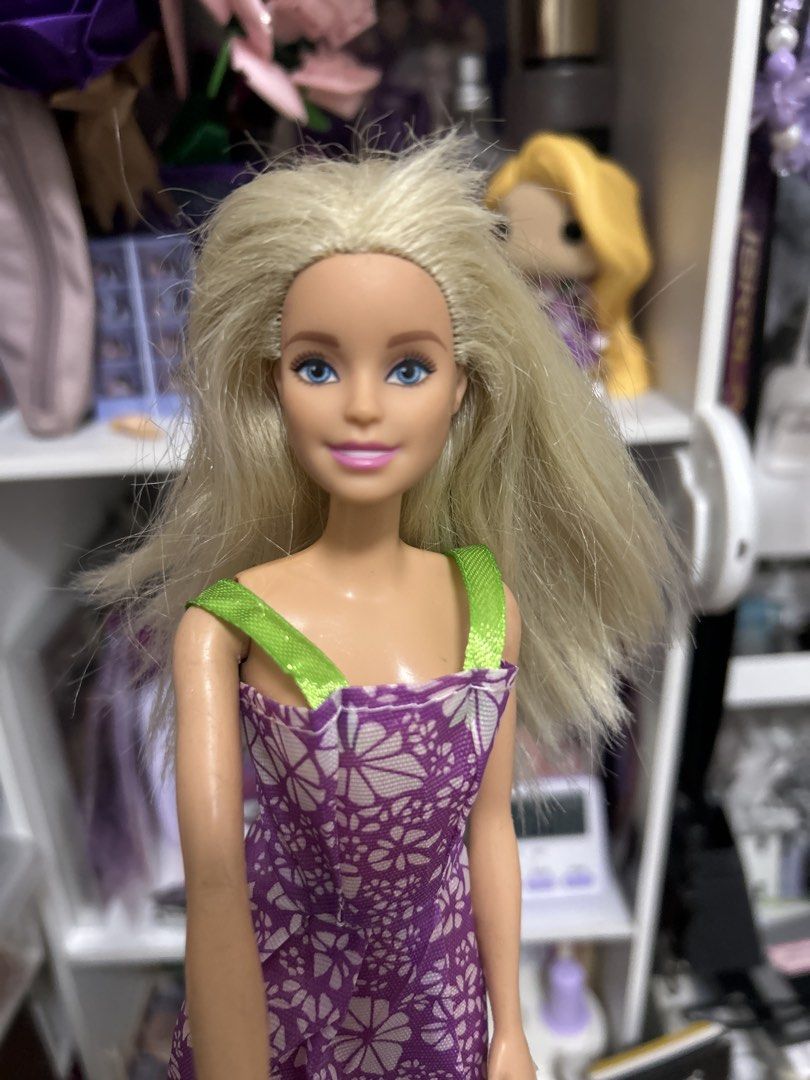 Barbie doll (Category: Kids Toys) located in Manila. Submitted by duhyahn (Listing ID 1464904917, Image 1). Description: - Doll: Classic Barbie with blue eyes and pink lips - Outfit: Purple dress featuring a white floral pattern and bright green straps - Hair: Blonde, has some frizz and needs a good brush - Body: Standard plastic construction - Condition: Fun piece, ideal for collectors or kids' playtime - Shipping: Ships fast from the Philippine