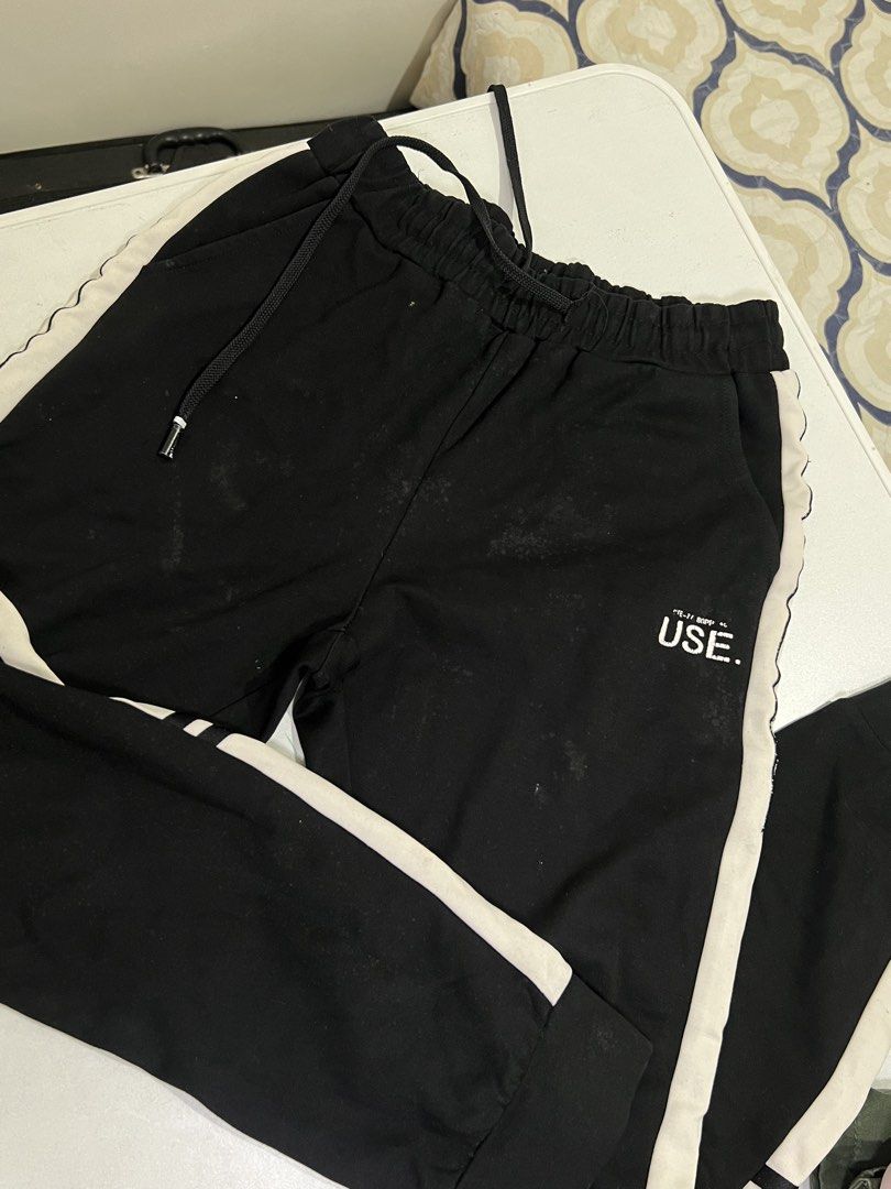 Black and White Jogger Sweatpants USE Text (Category: Joggers) located in Manila. Submitted by sennisen (Listing ID 1464922317, Image 2). Description: - Color: Black with white side stripes and text graphic near the pocket - Fit: Elastic waistband with adjustable black drawstring and cuffed ankles - Material: Soft, comfortable fabric ideal for everyday lounge wear - Condition: Noticeable stains and marks on the front thigh areas (priced according