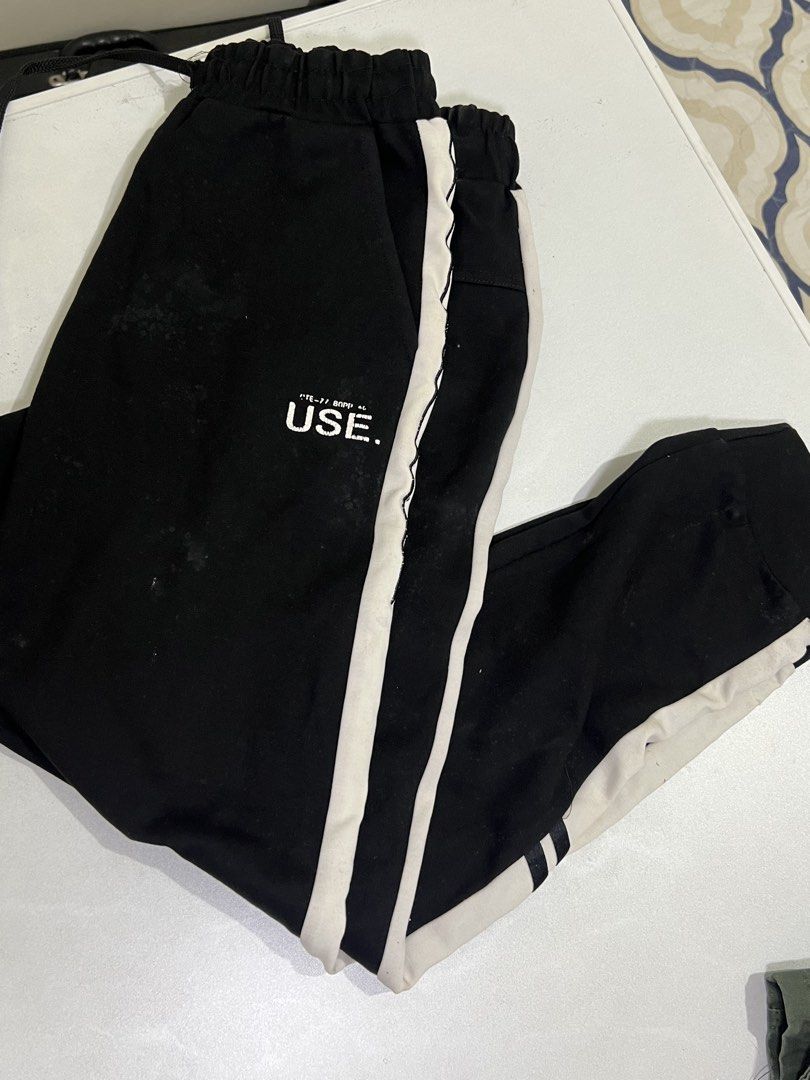 Black and White Jogger Sweatpants USE Text (Category: Joggers) located in Manila. Submitted by sennisen (Listing ID 1464922317, Image 1). Description: - Color: Black with white side stripes and text graphic near the pocket - Fit: Elastic waistband with adjustable black drawstring and cuffed ankles - Material: Soft, comfortable fabric ideal for everyday lounge wear - Condition: Noticeable stains and marks on the front thigh areas (priced according