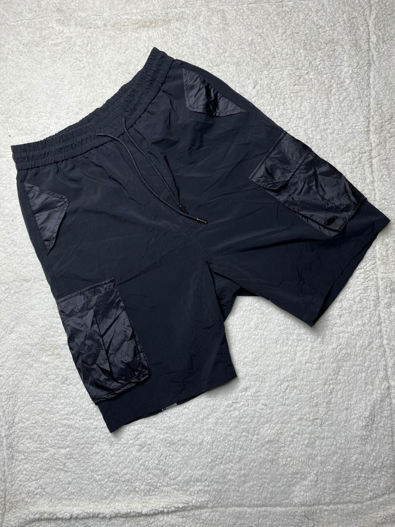 Black Nylon Cargo Shorts with Drawstring and Branding (Category: Shorts) located in Leyte. Submitted by carlthriftwearapparel (Listing ID 1464821122, Image 3). Description: - Color: Black - Material: Lightweight nylon, clean and ready to wear - Fit: Regular fit with elastic waistband and adjustable drawstring - Pockets: Multiple utility pockets with shiny dark fabric flaps plus a back zipped pocket - Details: Branded logo patch and striped tape w