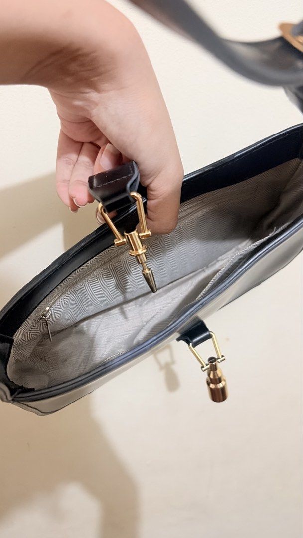 Black shoulder bag with gold hardware (Category: Shoulder Bags) located in Cagayan de Oro. Submitted by preloved_54 (Listing ID 1464894921, Image 1). Description: - Color & Style: Classic black structured shoulder bag - Hardware: Elegant gold accents with unique front and strap drop pendant closures - Interior: Stylish grey patterned fabric lining with a convenient inner zip pocket - Condition: Clean interior, gently handled and well-maintained -