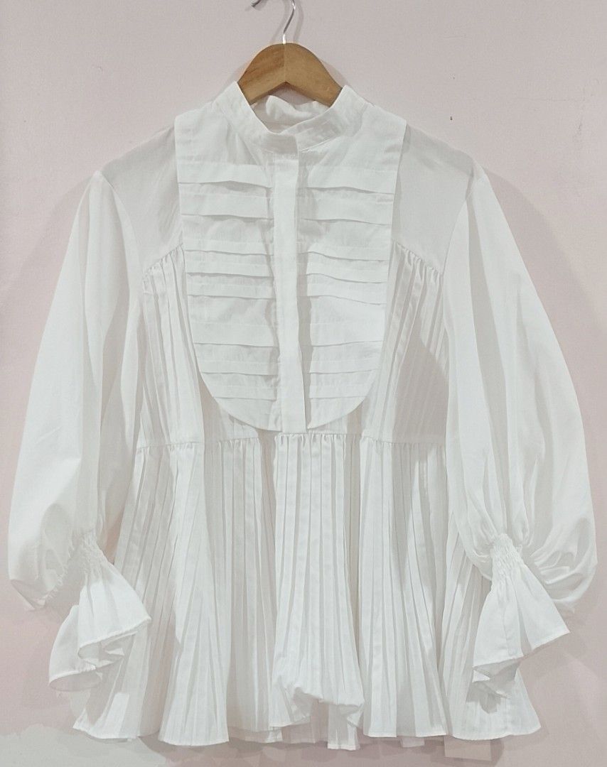 BNWT SNIDEL white Pintuck Frill Tunic Blouse (Category: Blouses) located in Cabanatuan. Submitted by miss.maia (Listing ID 1464847608, Image 1). Description: SNIDEL Pintuck Frill Tunic Blouse This romantic, vintage-inspired white top features a banded high-neck collar, a pleated bib-front panel with stitched accents, and dramatic, voluminous balloon sleeves that taper down into tiered ruffle cuffs. The lower half of the shirt is styled with verti