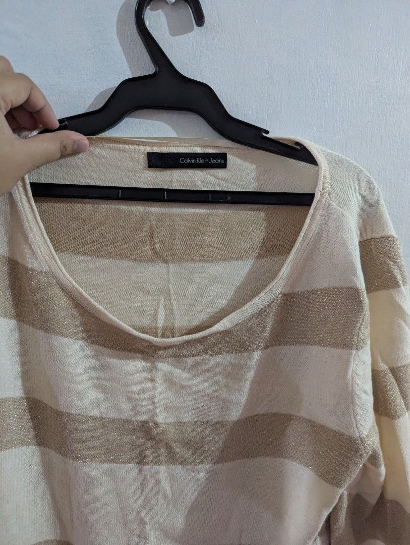 Calvin Klein Jeans Striped Glitter Sweater (Category: Longsleeves) located in Marikina City. Submitted by berabizz (Listing ID 1464888373, Image 2). Description: - Brand: Calvin Klein Jeans - Color: Cream and gold stripes with shimmering metallic thread - Neckline: Scoop neck - Sleeves: Long sleeves - Fit: Relaxed fit with soft knit fabric - Details: Small metal logo plate near the bottom hem - Style: Great layering piece for cooler weather.