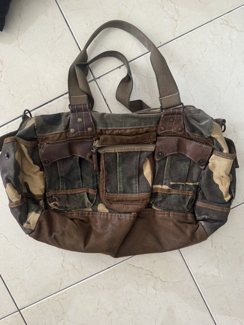 Camouflage Canvas and Brown Leather Utility Bag (Category: Luxury Bags & Wallets) located in Makati City. Submitted by lumpiawrapper (Listing ID 1464821744, Image 1). Description: - Style: Rugged military-inspired utility duffel - Material: Durable green camouflage canvas with brown faux leather trim and bottom panel - Features: Sturdy carry handles, multiple exterior pockets with snap buttons and zippers - Capacity: Spacious interior ideal for g