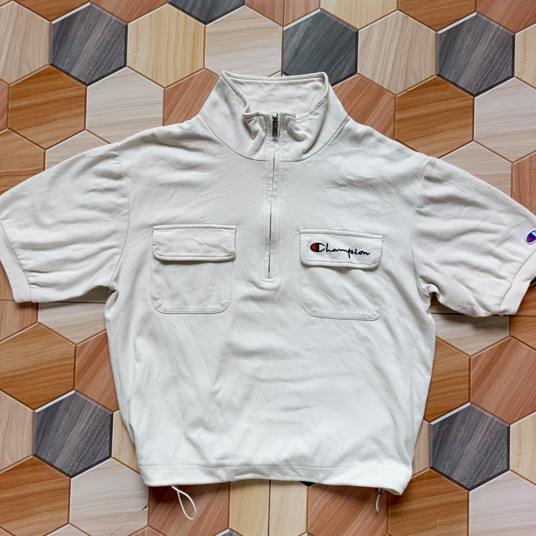 Champion White Half-Zip Short Sleeve Top Medium (Category: Shirts) located in Manila. Submitted by caps08 (Listing ID 1464883450, Image 1). Description: - Brand: Champion - Style: Half-zip short sleeve top with mock neck collar - Size: Medium (M) - Color: White - Features: Dual front flap pockets, adjustable drawstring hem - Branding: Embroidered Champion script logo on right chest pocket and small patch on left sleeve.