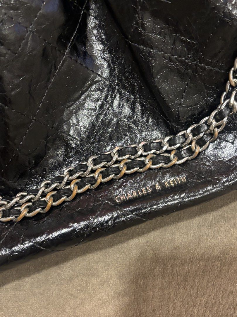 Charles & Keith Black Quilted Chain Shoulder Bag (Category: Shoulder Bags) located in Andop. Submitted by pinkmatcha0715 (Listing ID 1464962610, Image 2). Description: - Brand: Charles & Keith - Style: Shoulder bag with edgy crinkled patent finish and quilted pattern - Straps: Double chain strap woven with black material - Hardware: Silver-toned with subtle stamped logo near the base - Interior: Open top design with an internal zip pocket lining 