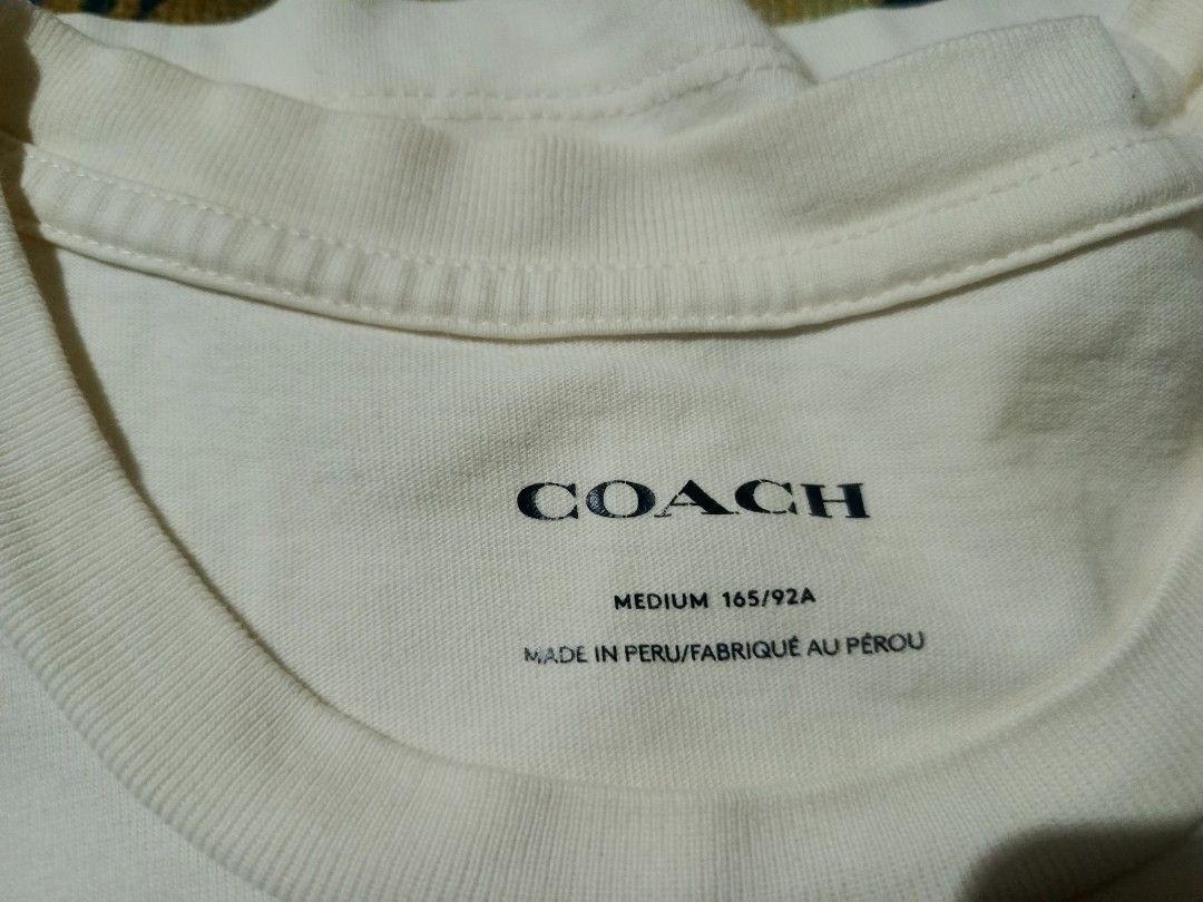 Coach Heart Logo T-Shirt (Category: Shirts) located in Manila. Submitted by thrift_sta.20 (Listing ID 1464869652, Image 2). Description: - Brand: Coach - Color: White - Size: Medium (165/92A) - Design: Signature monogram background in a square, big pink heart, and vertical Coach logo on the chest - Neckline: Classic crew neck - Origin: Made in Peru - Condition: Clean fabric, easy everyday wear - Mode of Payment: GCash - Shipping: Ships nationwide