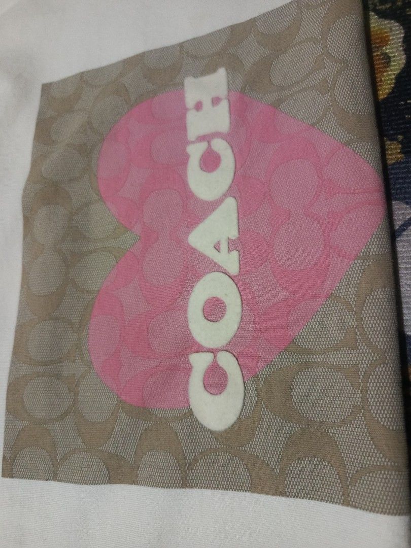 Coach Heart Logo T-Shirt (Category: Shirts) located in Manila. Submitted by thrift_sta.20 (Listing ID 1464869652, Image 3). Description: - Brand: Coach - Color: White - Size: Medium (165/92A) - Design: Signature monogram background in a square, big pink heart, and vertical Coach logo on the chest - Neckline: Classic crew neck - Origin: Made in Peru - Condition: Clean fabric, easy everyday wear - Mode of Payment: GCash - Shipping: Ships nationwide