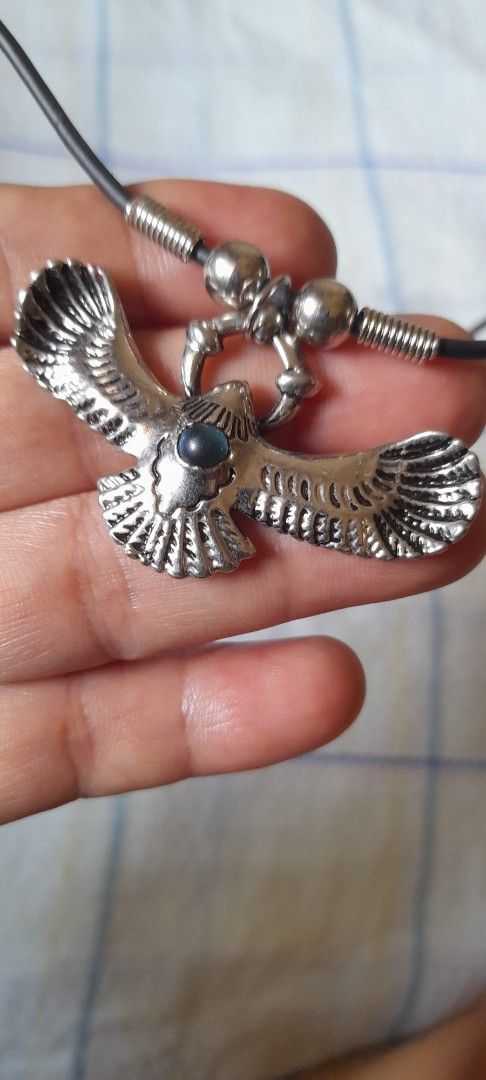 Eagle Pendant Necklace with Black Cord (Category: Necklaces) located in Bocaue. Submitted by marajapansurplus (Listing ID 1464772351, Image 1). Description: - Design: Silver-toned metal eagle pendant with textured wings and a dark central stone - Closure: Black cord choker with spring ring clasp - Size: Standard choker length - Condition: Hardware shows minor wear on the back side - Style: Great statement piece for casual outfits.
