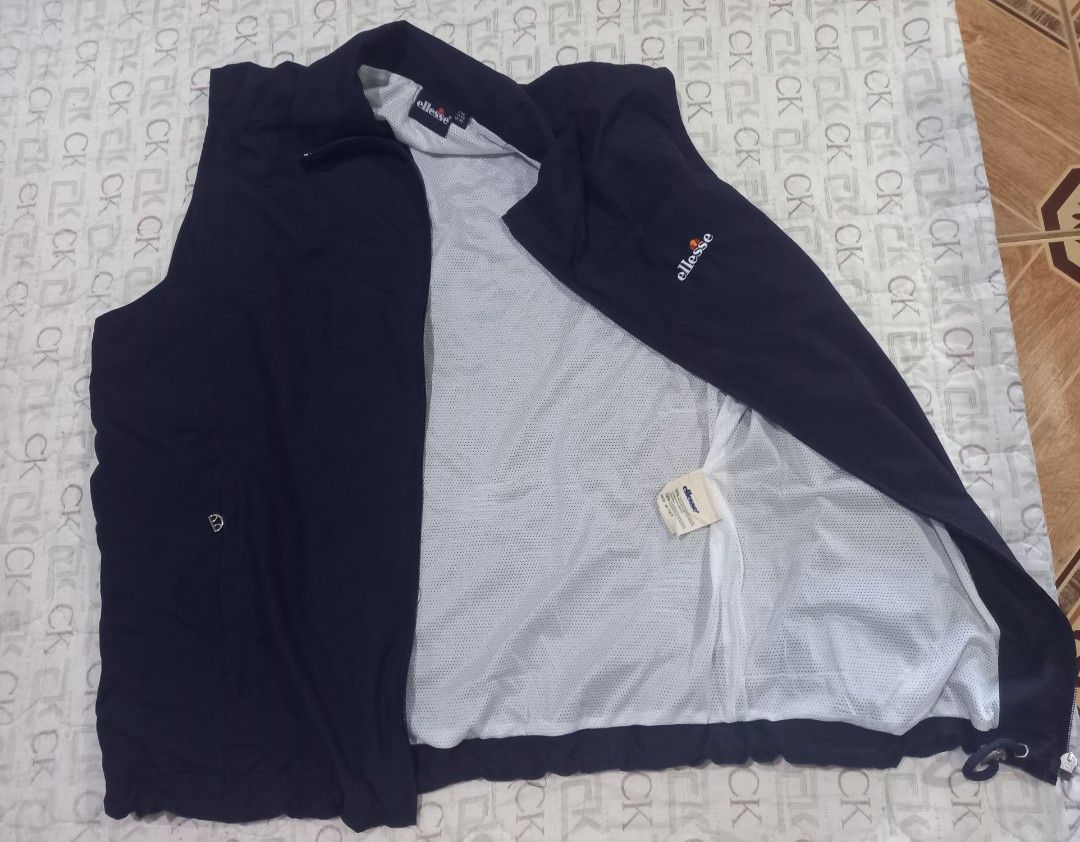 Ellesse navy blue sleeveless zip-up vest jacket (Category: Vests) located in Baguio. Submitted by jiannisthriftfits (Listing ID 1464954285, Image 3). Description: - Color: Dark navy blue - Brand: Ellesse (embroidered logo on left chest) - Design: Full zip front closure with a high collar - Lining: Breathable white mesh inner lining - Pockets: Secure zipped pockets on both sides - Fit: Adjustable drawstring hem at the bottom - Condition: Clean, li