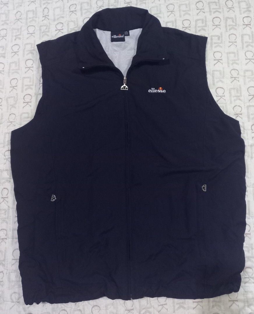 Ellesse navy blue sleeveless zip-up vest jacket (Category: Vests) located in Baguio. Submitted by jiannisthriftfits (Listing ID 1464954285, Image 1). Description: - Color: Dark navy blue - Brand: Ellesse (embroidered logo on left chest) - Design: Full zip front closure with a high collar - Lining: Breathable white mesh inner lining - Pockets: Secure zipped pockets on both sides - Fit: Adjustable drawstring hem at the bottom - Condition: Clean, li