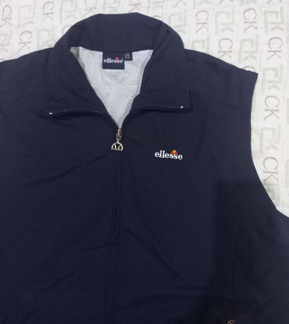 Ellesse navy blue sleeveless zip-up vest jacket (Category: Vests) located in Baguio. Submitted by jiannisthriftfits (Listing ID 1464954285, Image 2). Description: - Color: Dark navy blue - Brand: Ellesse (embroidered logo on left chest) - Design: Full zip front closure with a high collar - Lining: Breathable white mesh inner lining - Pockets: Secure zipped pockets on both sides - Fit: Adjustable drawstring hem at the bottom - Condition: Clean, li