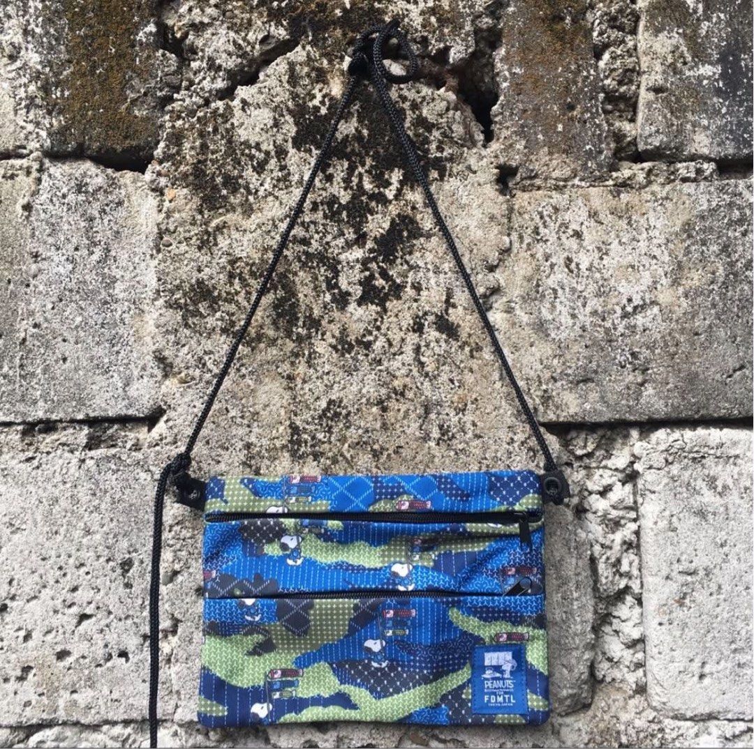 FDMTL x Peanuts (Category: Sling Bags) located in Rizal. Submitted by timelessfinds89_ (Listing ID 1464916755, Image 1). Description: - Brand: FDMTL x Peanuts Collaboration - Design: Blue camouflage with iconic Snoopy and carp streamer graphics - Compartments: Secure main zip opening plus two front zip pockets - Interior: Clean dark blue lining - Strap: Comfortable, adjustable black cord strap - Details: Signature woven brand patch on the lower f