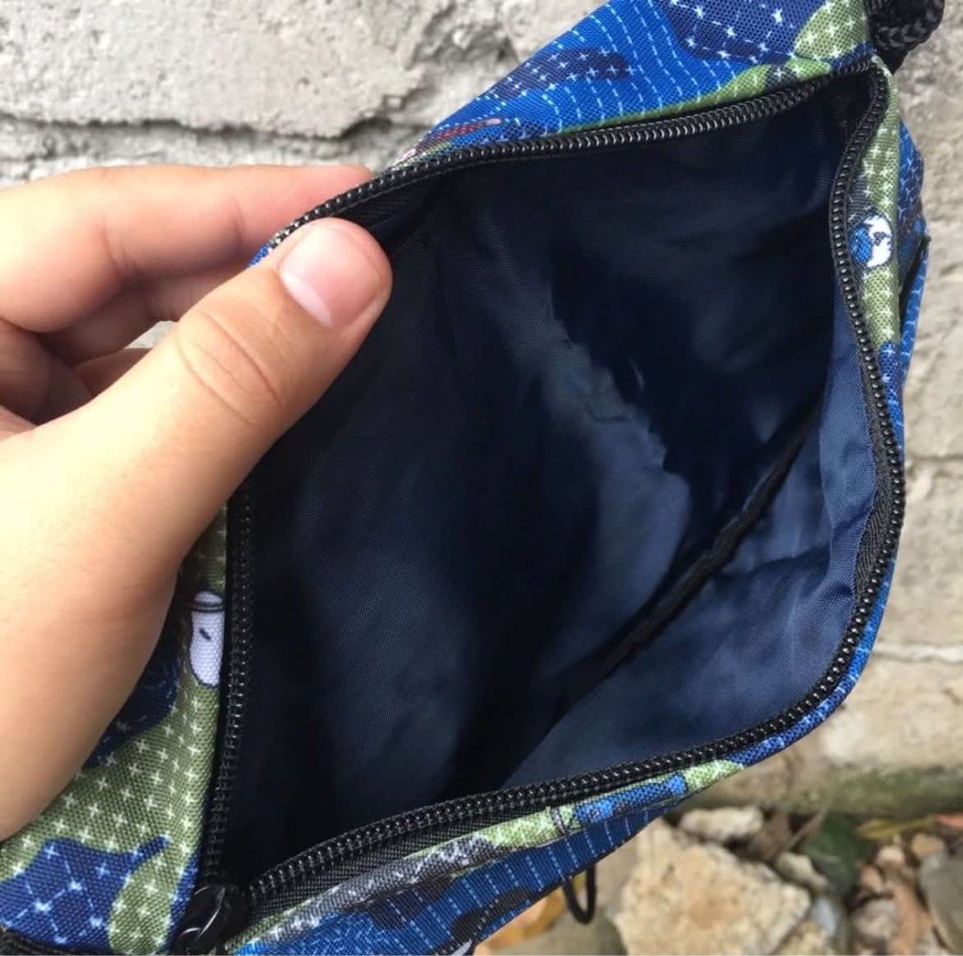 FDMTL x Peanuts (Category: Sling Bags) located in Rizal. Submitted by timelessfinds89_ (Listing ID 1464916755, Image 2). Description: - Brand: FDMTL x Peanuts Collaboration - Design: Blue camouflage with iconic Snoopy and carp streamer graphics - Compartments: Secure main zip opening plus two front zip pockets - Interior: Clean dark blue lining - Strap: Comfortable, adjustable black cord strap - Details: Signature woven brand patch on the lower f